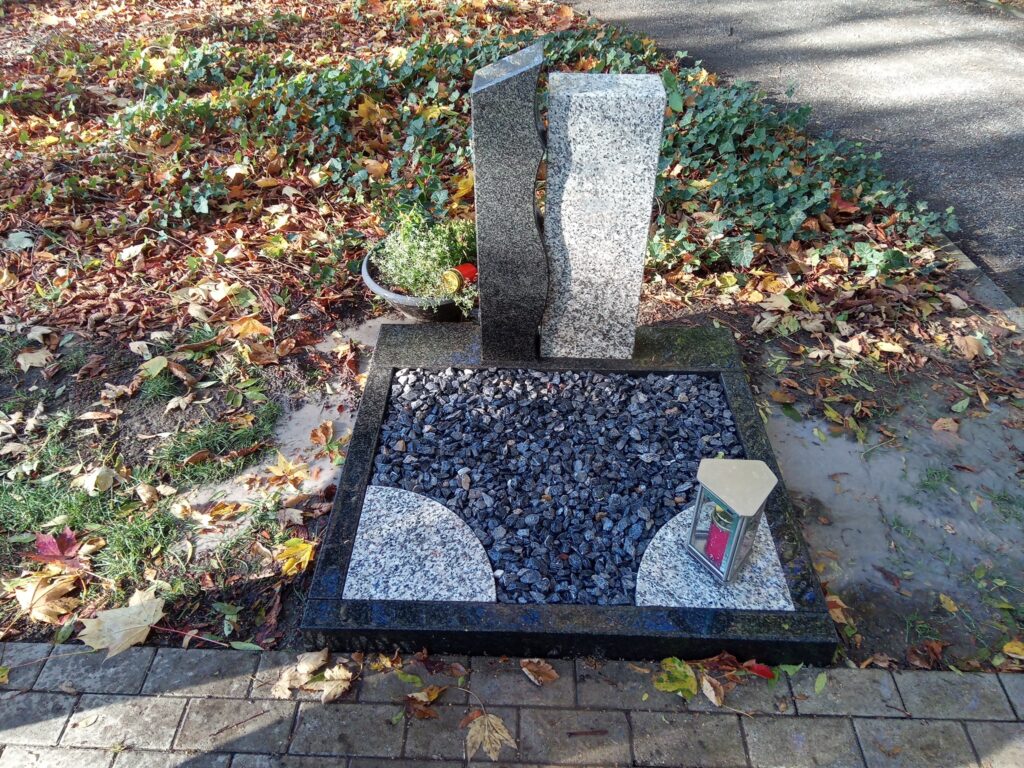 Zweiteiliges Grabmal aus hellem und dunklem Granit mit Kiesbett im Herbst